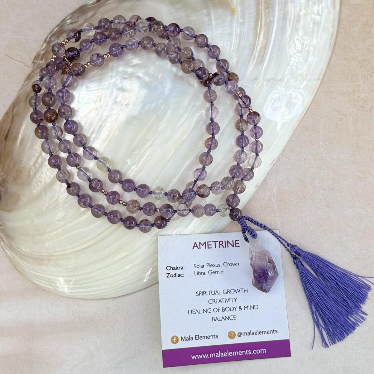 A multi-strand amethyst beaded mala necklace with a lilac cord and tassel, displayed on a white shell with a product card that reads 'AMETRINE' and shows the brand 'Mala Elements'.