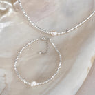 A silver beaded necklace and matching bracelet set with a single white keshi pearl at it's center. 