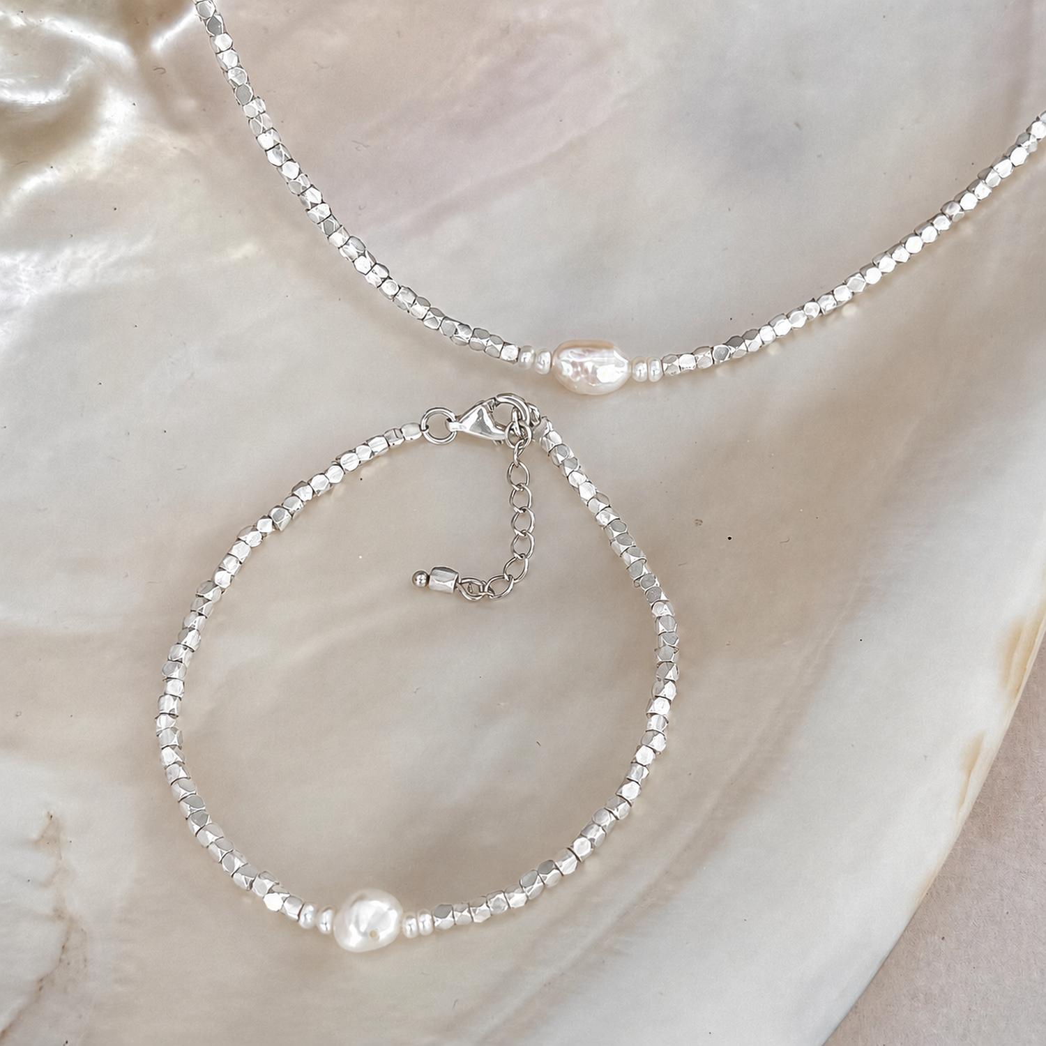 A silver beaded necklace and matching bracelet set with a single white keshi pearl at it's center. 