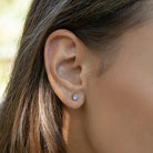 A close-up of a person's ear wearing a small pink amethyst round stud earring in solid gold