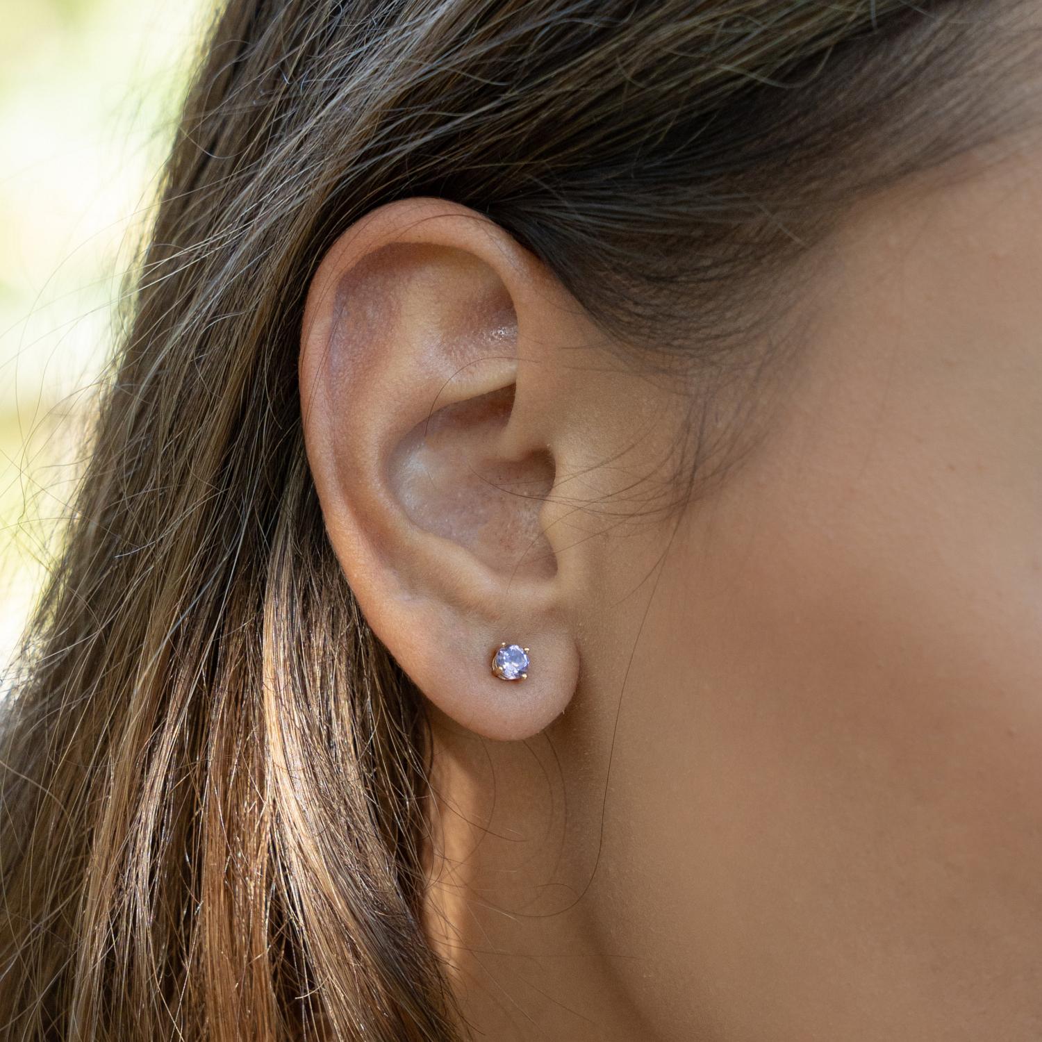 A close-up of a person's ear wearing a small pink amethyst round stud earring in solid gold