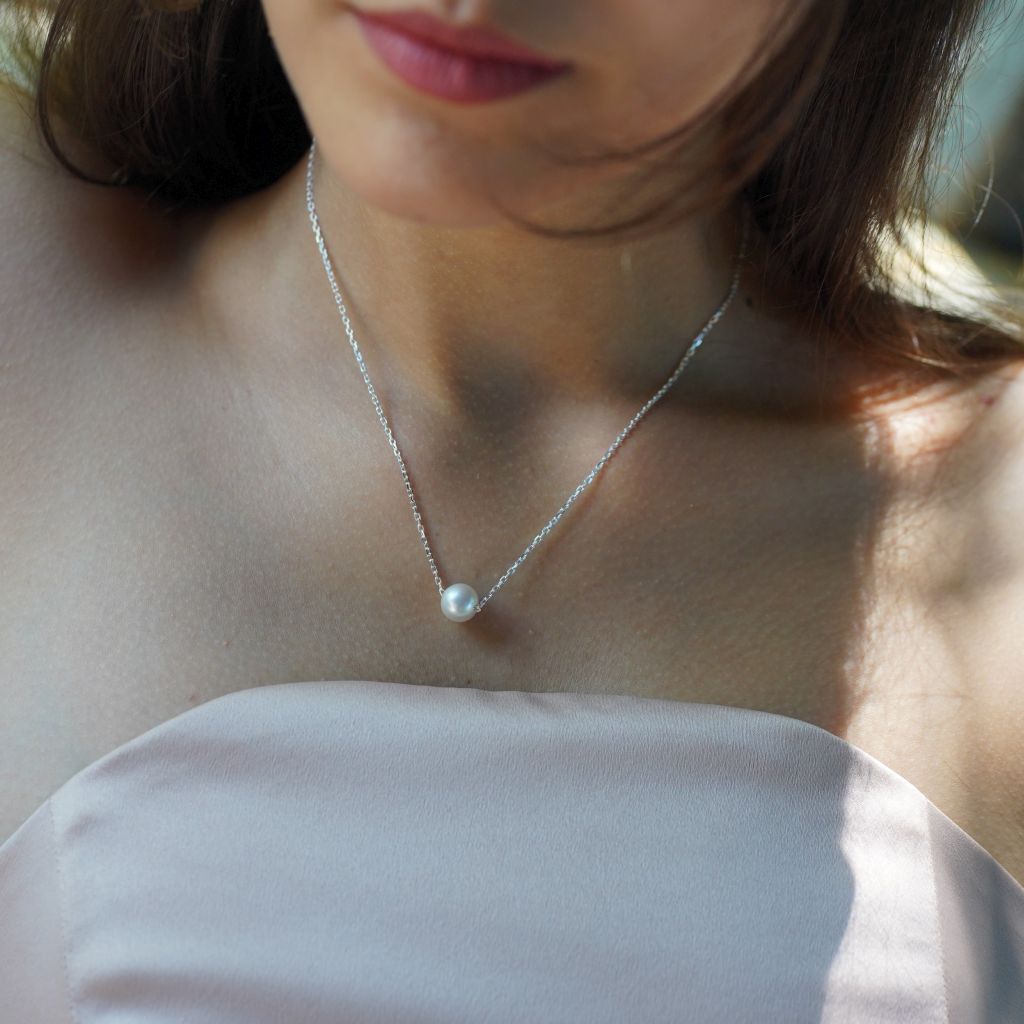 A woman wearing a sterling silver necklace with a single white South Sea pearl pendant.