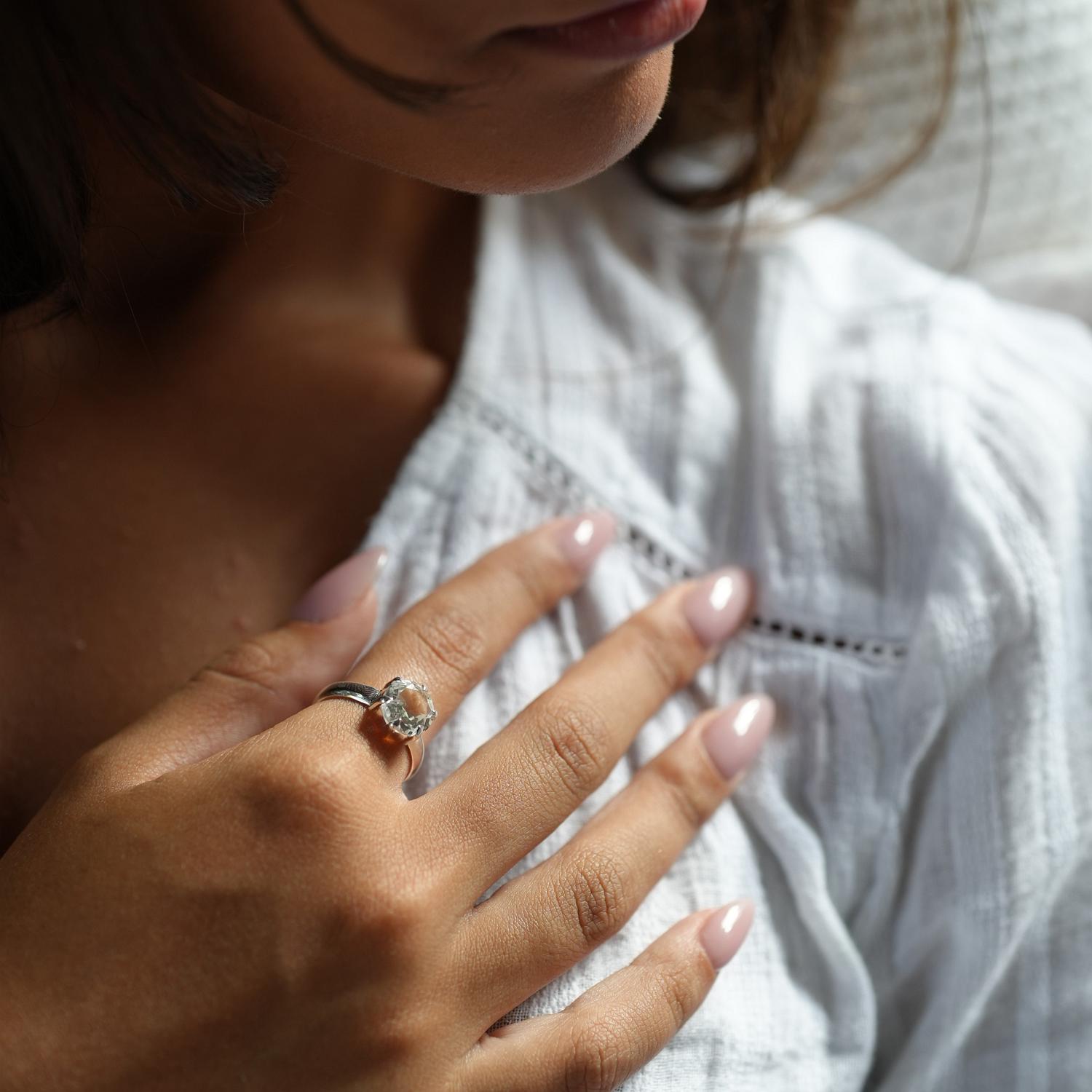 A close-up lifestyle shot of a woman wearing a silver ring with a round white topaz gemstone on her finger.